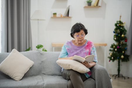 Senior Asian Woman Enjoying a Peaceful Reading Session on a Cozy Sofa in a Bright Living Room with Natural Light and Minimalist Decorの写真素材
