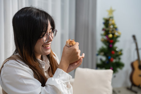 Joyful woman holding a cute pet hamster in a cozy home with festive Christmas tree and warm decorations in the background during holiday seasonの写真素材