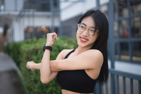 A young woman stretches outdoors in an urban environment, dressed in stylish black sportswear, embodying health and fitness with a confident attitude.の写真素材