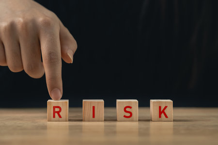Focused Hand Pointing at Wooden Blocks Spelling Risk in a Dark Setting, Symbolizing Business Challenges and Decision-Making in Uncertain Environmentsの写真素材