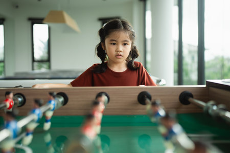 Young girl playing foosball with concentration in a bright and modern game room featuring large windows and a relaxed atmosphereの写真素材