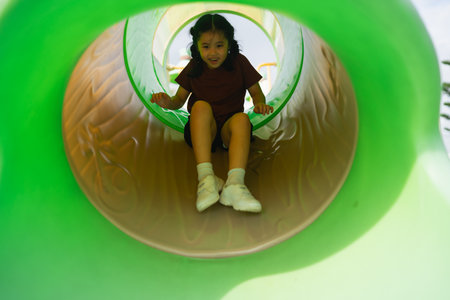 Child slides down colorful playground tube, happy expression, sunny day, outdoor fun, childhood adventure, playful moment captured in vibrant settingの写真素材