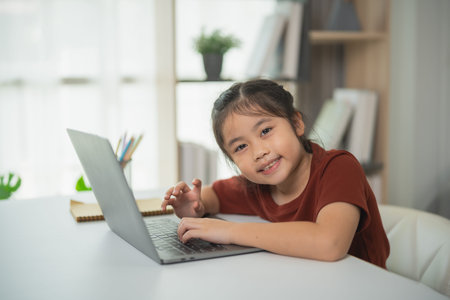 Smiling Asian girl working on laptop at home, engaging in creative activities, enjoying online...