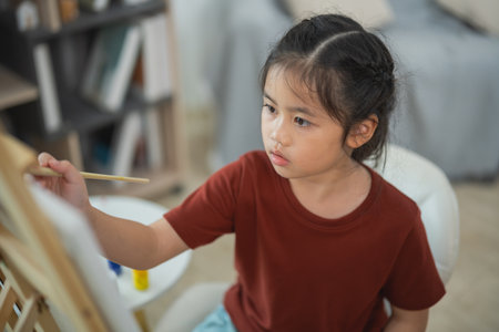 Young Girl Engaged in Creative Painting Hobby at Home Indoors, Expressing Artistic Talent with Brush and Canvas, Nurturing Imagination and Skillsの写真素材