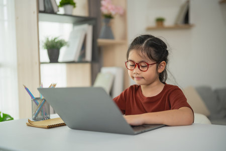 Young girl with glasses working on laptop at home, focused on study activities, modern interior,...