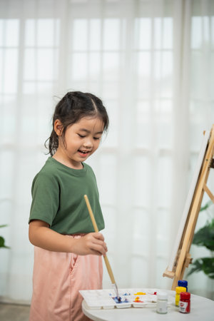 Happy young girl enjoying creativity while painting on canvas at home with colorful paints and smile under bright natural light in a cozy roomの写真素材