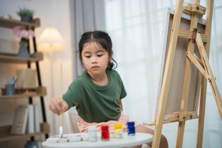 Young girl engages in creative expression through painting at home, showcasing passion for art and growth in a cozy, inspiring environment.の写真素材