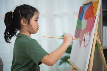 Young girl painting on canvas with bright colors indoors, focused on creative expression, artistic development and imagination in home settingの写真素材