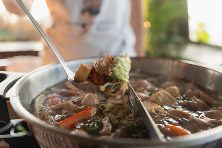 Delicious and Flavorful Asian Hot Pot with Fresh Vegetables, Tender Meat, and Aromatic Broth Served in a Modern Restaurant Settingの写真素材