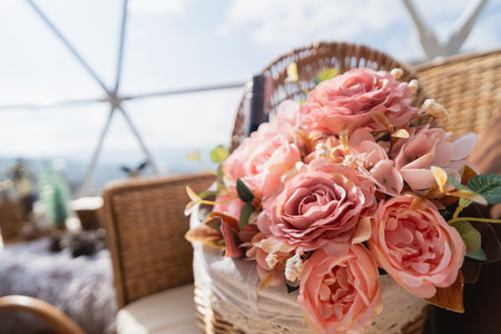 Beautiful arrangement of pink and cream flowers in a woven basket placed indoors surrounded by natural light and a scenic view of the landscapeの写真素材