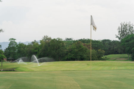 Serene Golf Course Landscape with Flag, Engaging Green Lawn, Water Sprinklers in Action, Summer Sky, Fresh Air and Tranquility of Natureの写真素材