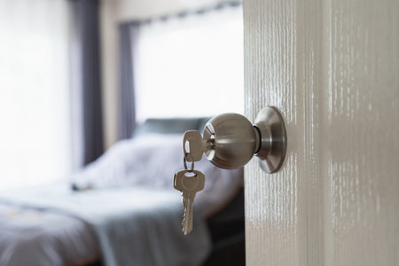 Modern Door Handle with Keys Hanging, Bright Bedroom Interior Revealing Soft Textiles, Natural Light Streaming Through Windowsの写真素材