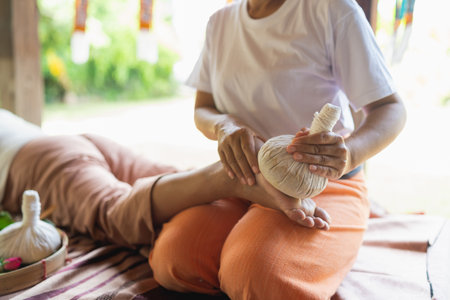 Traditional Thai Herbal Compress Massage Treatment for Relaxation and Wellness in Peaceful Spa Setting with Natural Lightの写真素材