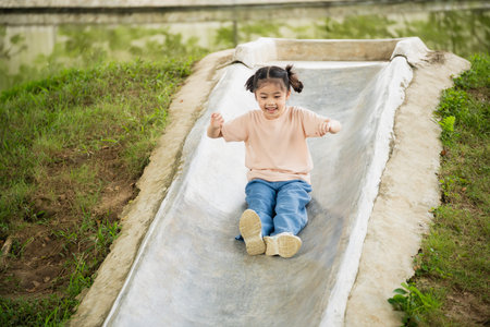 Happy child sliding down a playground slide in a park, enjoying outdoor playtime, smiling and having...