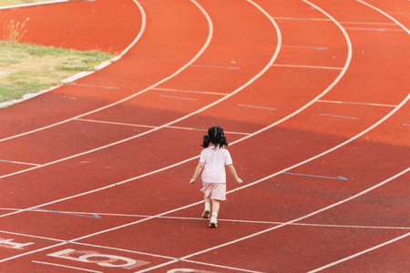 A Young Girl Walks Alone on a Red Outdoor Track While Leaving Footprints Behind, Symbolizing Journey...