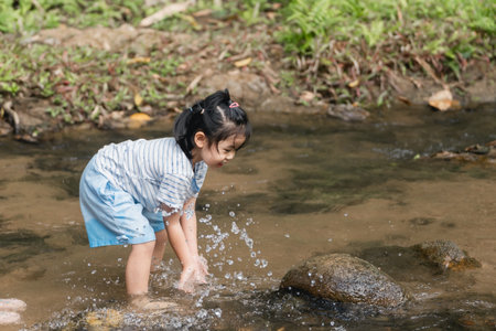 Young Child Playing in Stream, Splashing Water, Enjoying Nature, Outdoor Fun, Child's Joy in River, Playful Scene, Summer Activities, Childhood Adventureの写真素材