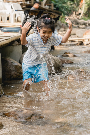 Joyful Child Playing and Splashing in Shallow Stream Water on a Sunny Day in Nature Surrounded by...
