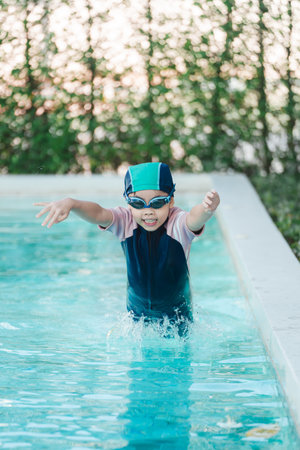 Child in Swim Cap and Goggles Splashing in Pool Water, Capturing Joyful Moment During Summer Swim Lesson in Bright Natural Light Settingの写真素材