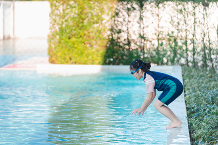 Young child preparing to dive into a refreshing pool water, wearing swim gear and goggles, sunny day with greenery in the background, summer fun at homeの写真素材