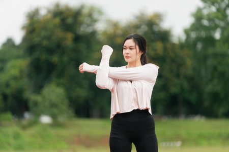Young female athlete stretching on outdoor track, preparing for workout session in natural environment, focused on fitness and wellness activities.の写真素材