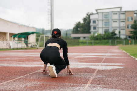 Female Athlete Preparing for Race on Track at Outdoor Stadium, Focus on Sprinting Posture with Determined Expression and Training Environmentの写真素材