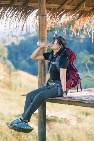 Relaxed Female Hiker Enjoys Refreshing Water Break While Sitting on Wooden Platform Surrounded by Lush Nature and Scenic Viewの写真素材