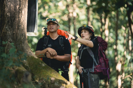 Two enthusiastic hikers exploring a lush green forest while discussing their outdoor adventure, wearing backpacks and preparing for a trek in natureの写真素材