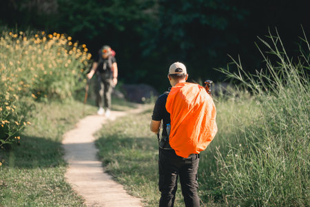 Hikers on Nature Trail Surrounded by Wildflowers and Greenery Exploring Beautiful Landscape on a Bright Sunny Dayの写真素材