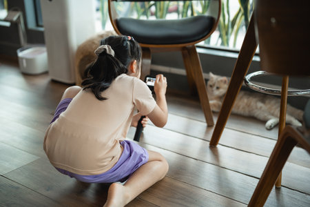 Young Child Captures Photo of Cat While Sitting on Floor in Cozy Indoor Space Surrounded by Modern Furniture and Natural Lightの写真素材