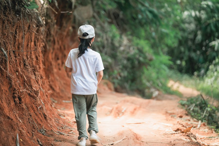 Child Walking Along Dirt Path in Lush Green Landscape, Casual Attire, Exploring Nature, Journey of Discovery, Outdoor Adventure, Peaceful Sceneの写真素材