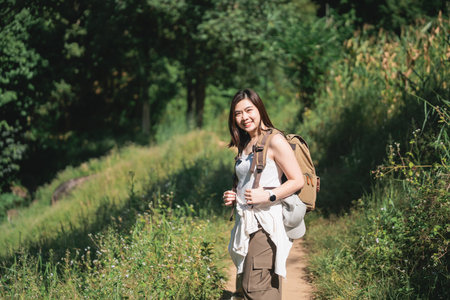 Young woman enjoying hiking adventure on a sunny day in nature, surrounded by greenery and vibrant plants on a scenic trailの写真素材