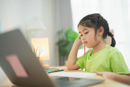 Young girl focusing on her homework with a laptop, colorful stationery, and a cozy study space,...