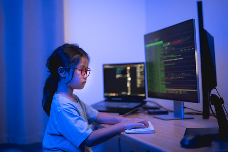 Young Girl Working on Computer in a Cozy Room with Blue Lighting, Focused on Programming and Learning Technology Skillsの写真素材