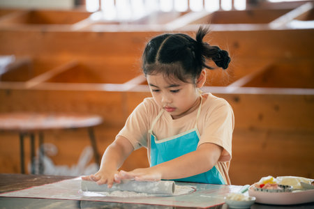 Young Girl Engaging in Creative Play While Rolling Dough at a Wooden Table in a Cozy Kitchen Settingの写真素材