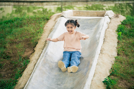 Happy young girl enjoying slide outdoors in a park, playful moments on a sunny day, childhood joy, carefree fun, laughter and excitement capturedの写真素材