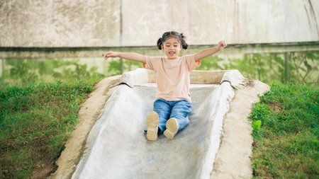 Joyful Child Sliding Down Playground Slide in Summer, Happy Expressions, Outdoor Fun, Playtime Activity, Nature Background, Smiling Girlの写真素材