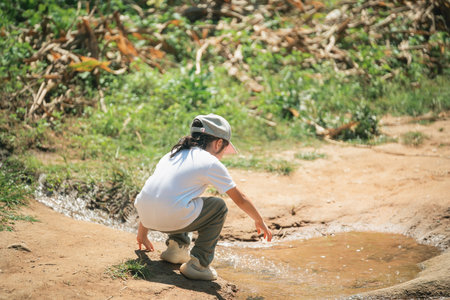 Child in Outdoor Environment Playing by Stream, Wearing Casual Clothing, Observing Water, Nature Exploration, Warm Weather, Summer Activities, Active Lifestyle, Joyful Momentの写真素材
