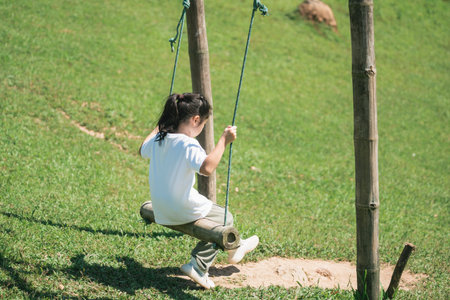 Child Joyfully Playing on a Swing in a Sunny Park Surrounded by Green Grass and Nature, Enjoying...