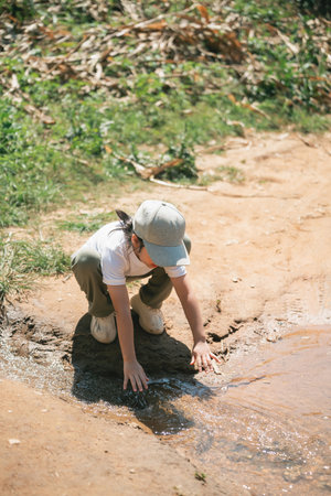 Child Exploring Nature by Stream Water, Touching Water Surface with Hands, Curiosity and Discovery in Natural Environment, Playful Outdoor Experienceの写真素材