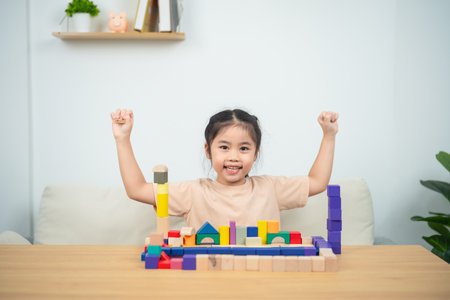 Joyful Child Celebrating Success with Colorful Building Blocks in a Bright and Inviting Indoor Spaceの写真素材