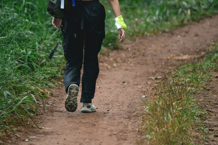 Person Walking on a Natural Trail Surrounded by Greenery with a Backpack and Sporty Outfit on a Sunny Day in a Forested Environmentの写真素材
