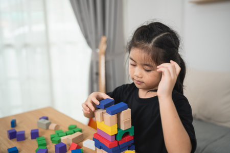 Young Child Engaged in Creative Play with Colorful Building Blocks in Cozy Indoor Space, Focused on Constructing Tower of Various Shapesの写真素材