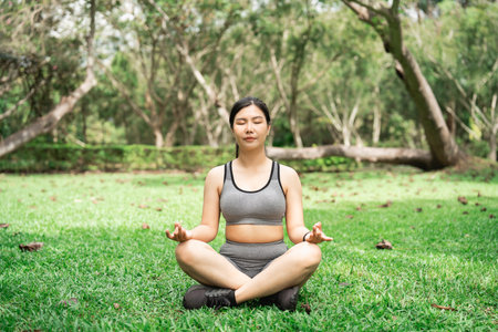 Young woman practicing yoga meditation in green park, surrounded by nature, focusing on mindfulness and tranquility in a serene atmosphereの写真素材