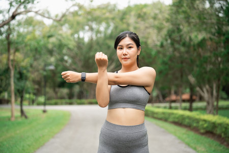 Fit woman stretching her arms outdoors in a park wearing athletic wear, promoting health and fitness lifestyle in a serene environmentの写真素材