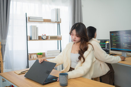Young women working in a modern office space, collaborating on laptops, with stylish furniture and soft lighting, creative environment for productivityの写真素材