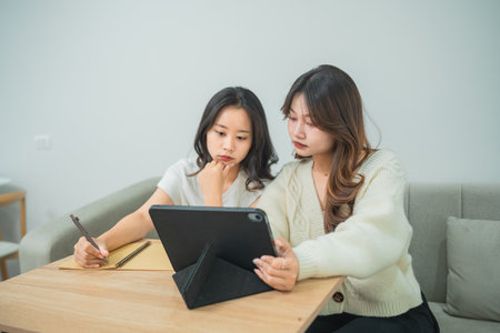 Two Young Women Engaged in a Creative Brainstorming Session at Home with Tablet, Notepad, and Pen for Ideas and Inspiration in Modern Interiorの写真素材