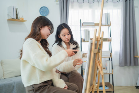 Two women discussing art techniques in a cozy indoor studio space with an easel and natural light, sharing creative inspiration and ideas calmlyの写真素材