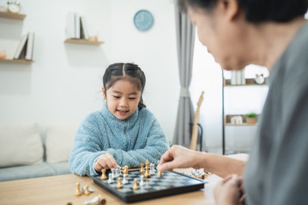 Young girl engages in a chess game with her grandmother in a cozy living room, showcasing bonding and learning through gameplay in a warm and inviting environment.の写真素材
