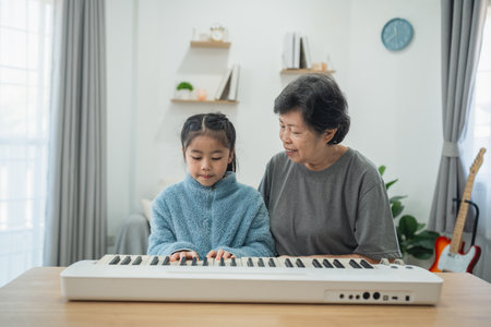 Heartwarming Moment of Grandmother Teaching Young Girl to Play Piano in Cozy Living Room Setting with Natural Light and Soft Decor Elementsの写真素材