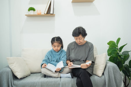 Grandmother and granddaughter reading together in cozy living room, enjoying quality time and fostering love for books and learning in home environmentの写真素材